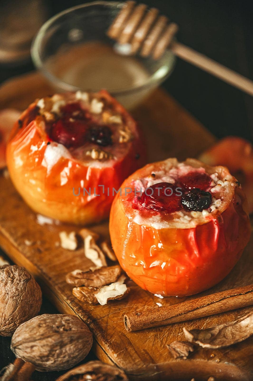 baked apples with cottage cheese with berries and nuts, topped with honey and sprinkled with cinnamon. on a wooden surface in a rustic style