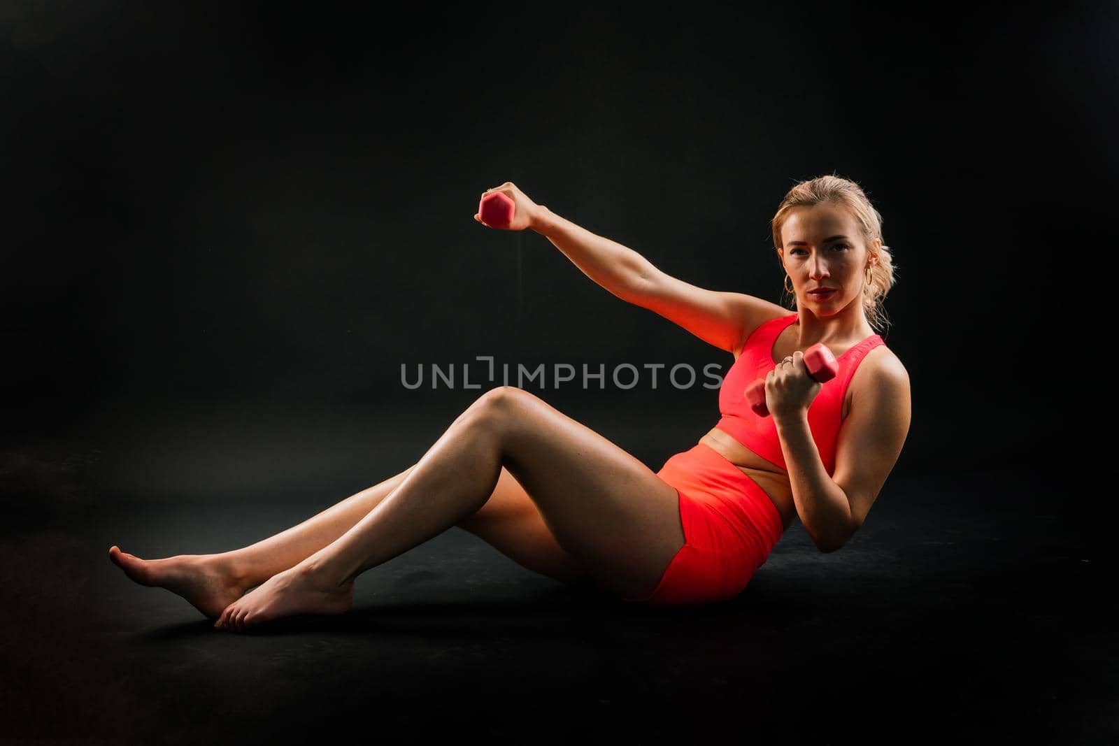 Beautiful female with dumbbells posing on studio background by Zelenin