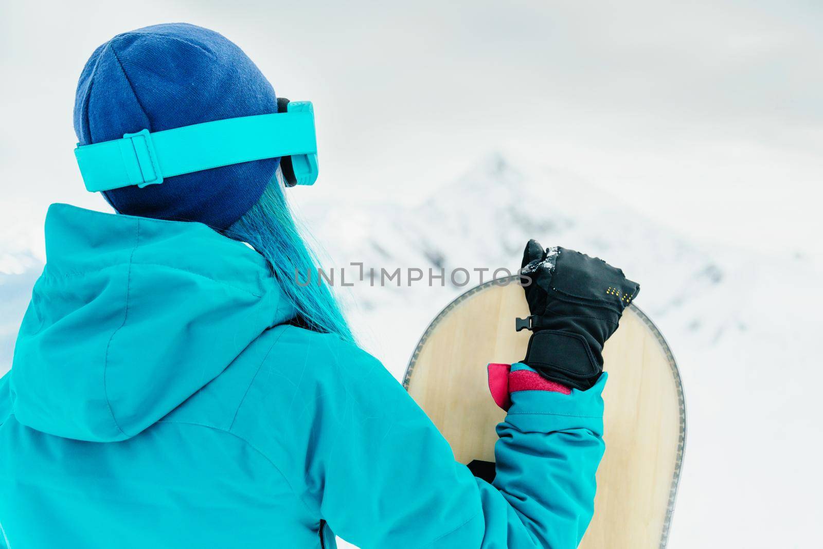 Unrecognizable young woman standing with snowboard in winter outdoor.