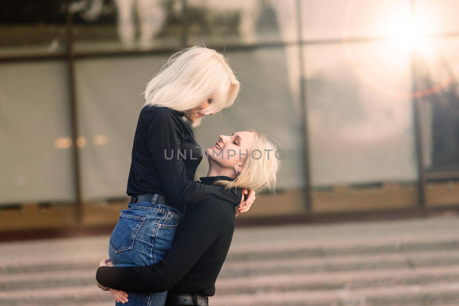 Two young females walking smiling embracing and kissing outdoor in the city by Zelenin