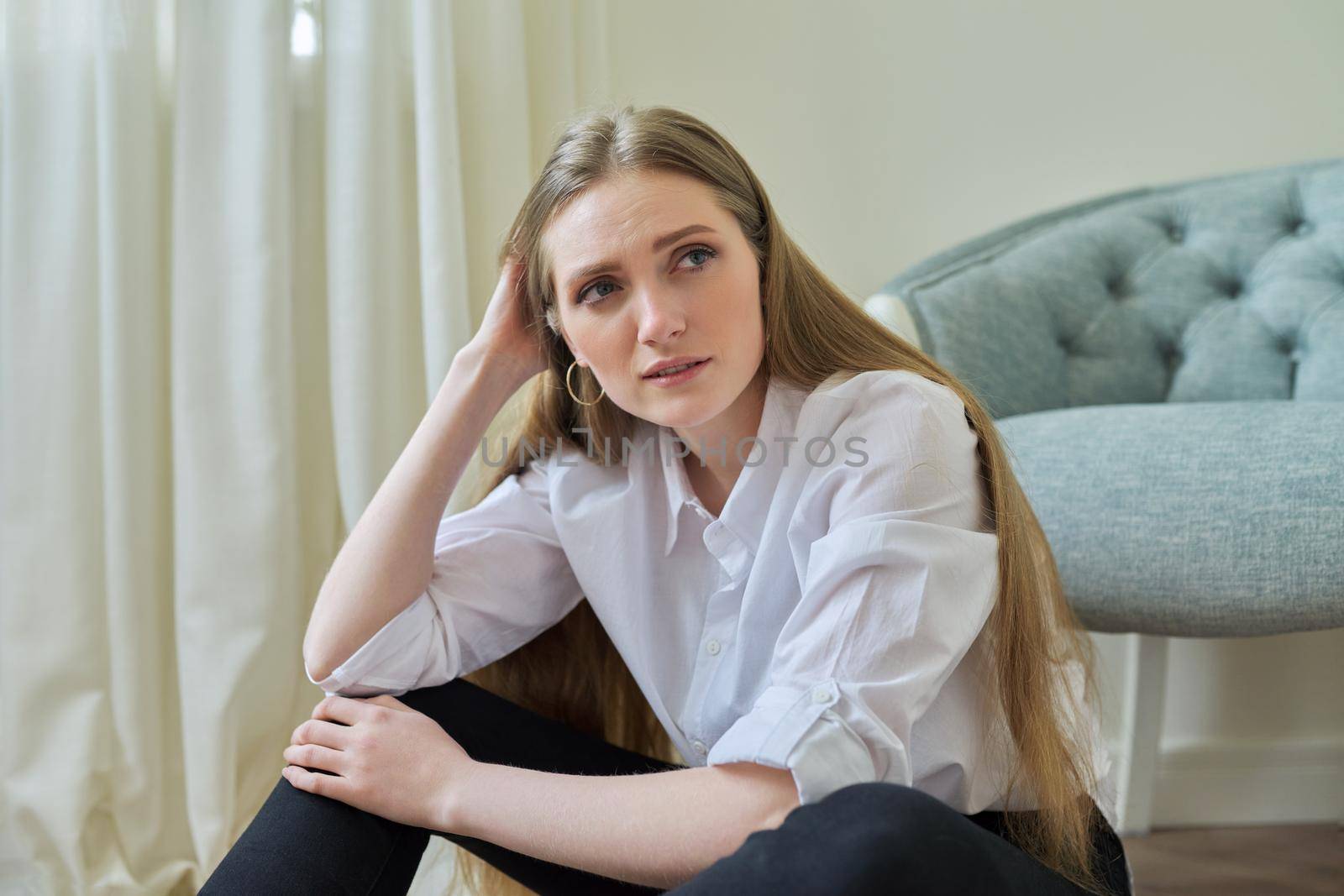 Upset crying young woman sitting at home on the floor. Negative emotions, stress, mental health, frustration, pain, people concept