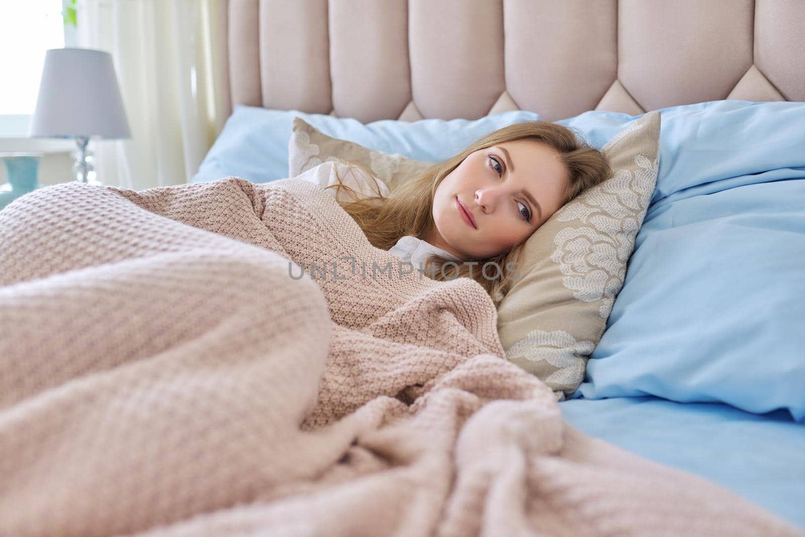 Young beautiful woman lying in bed during the day, covered with a knitted blanket. Daytime sleep, relaxation, beauty and health, sleep concept