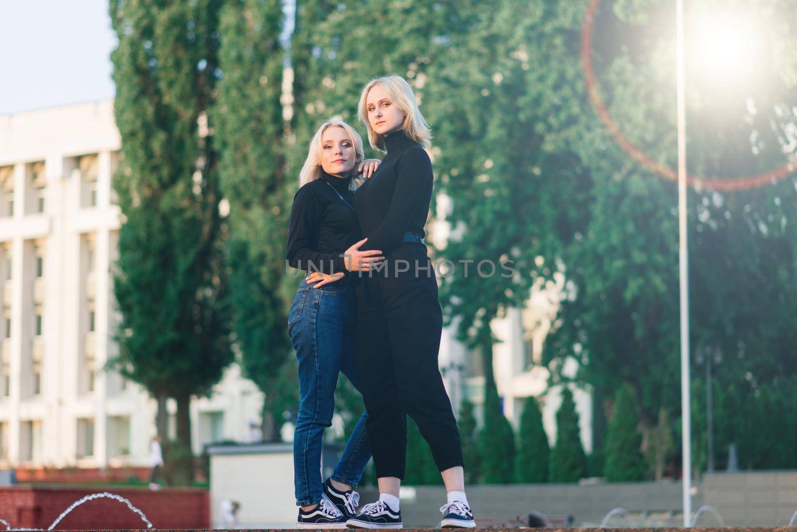 Two young females walking smiling embracing and kissing outdoor in the city by Zelenin