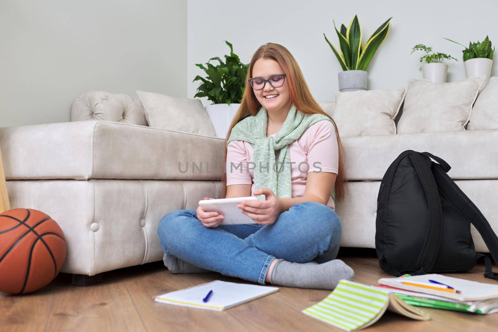 Portrait of teenage girl 12, 13 years old sitting at home on floor with school books, digital tablet. Online studies, e-education, resting schoolgirl using Internet modern digital technologies gadgets