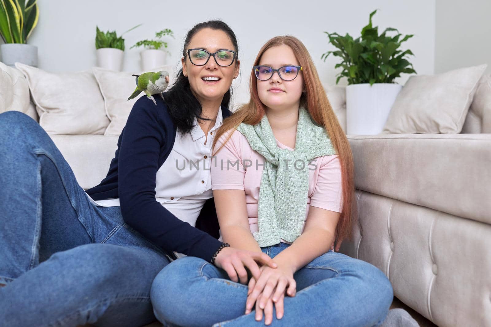 Friendly cheerful family, portrait of mom and teenage daughter, with green pet quaker parrot on woman's shoulder