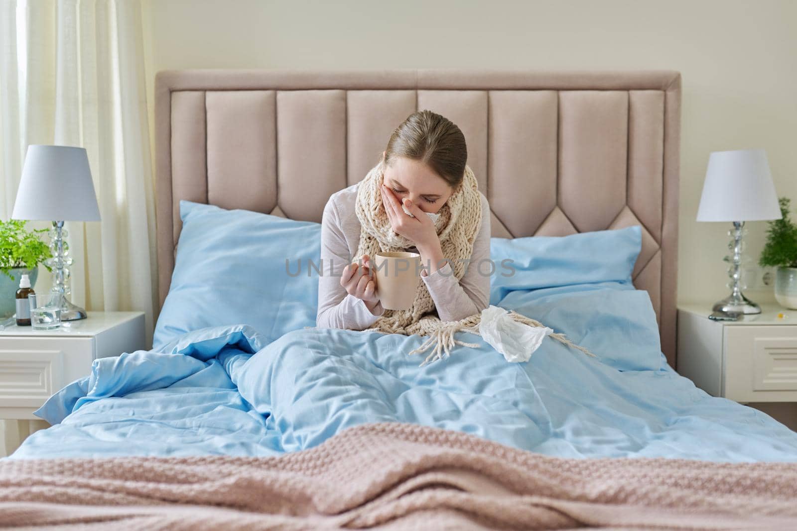 Sick young woman at home in bed with a cup of hot drink and a handkerchief. Cold symptoms, flu season, virus