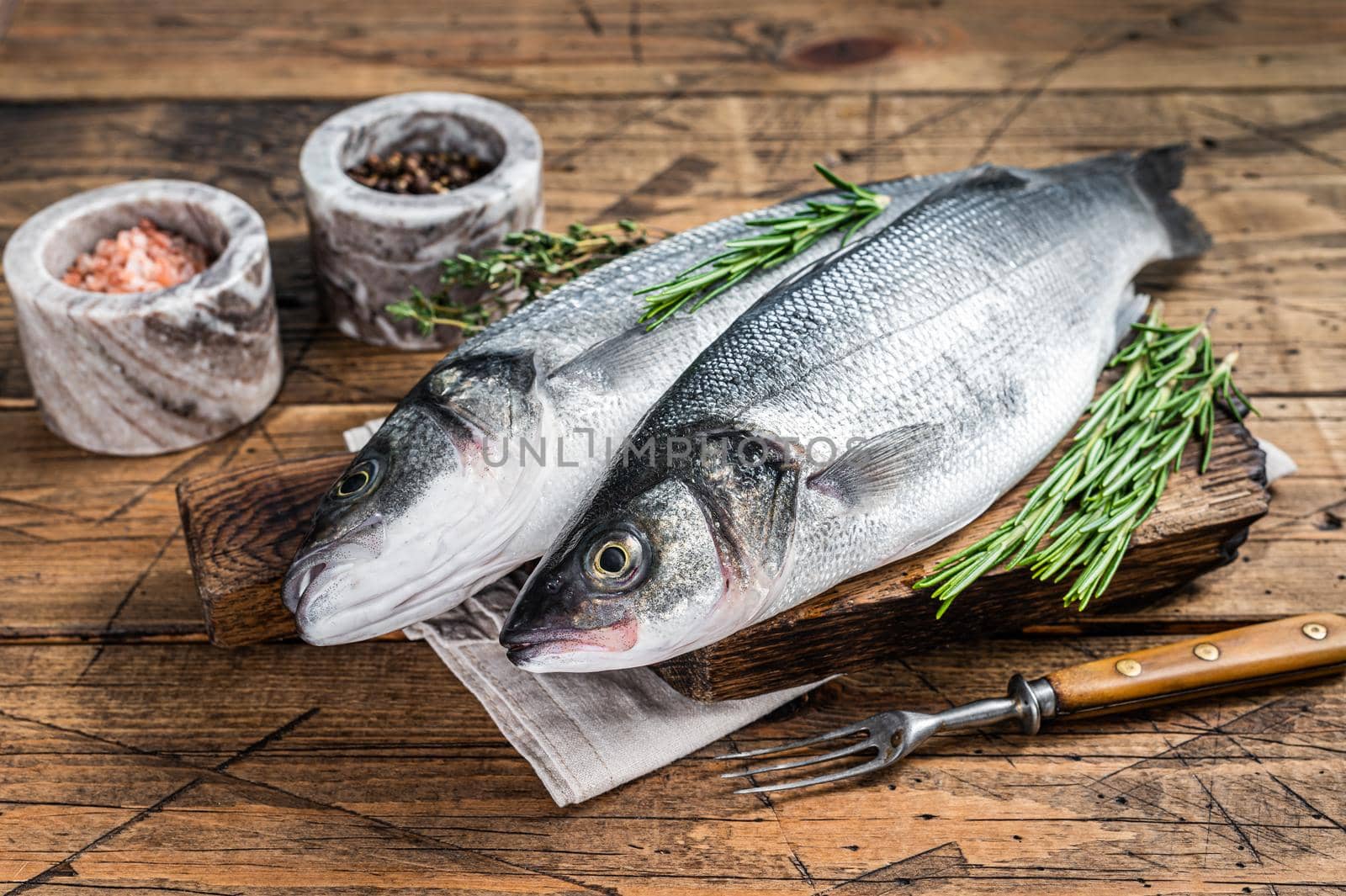 Seabass fresh raw fish on a wooden cutting board with rosemary. wooden background. Top view.