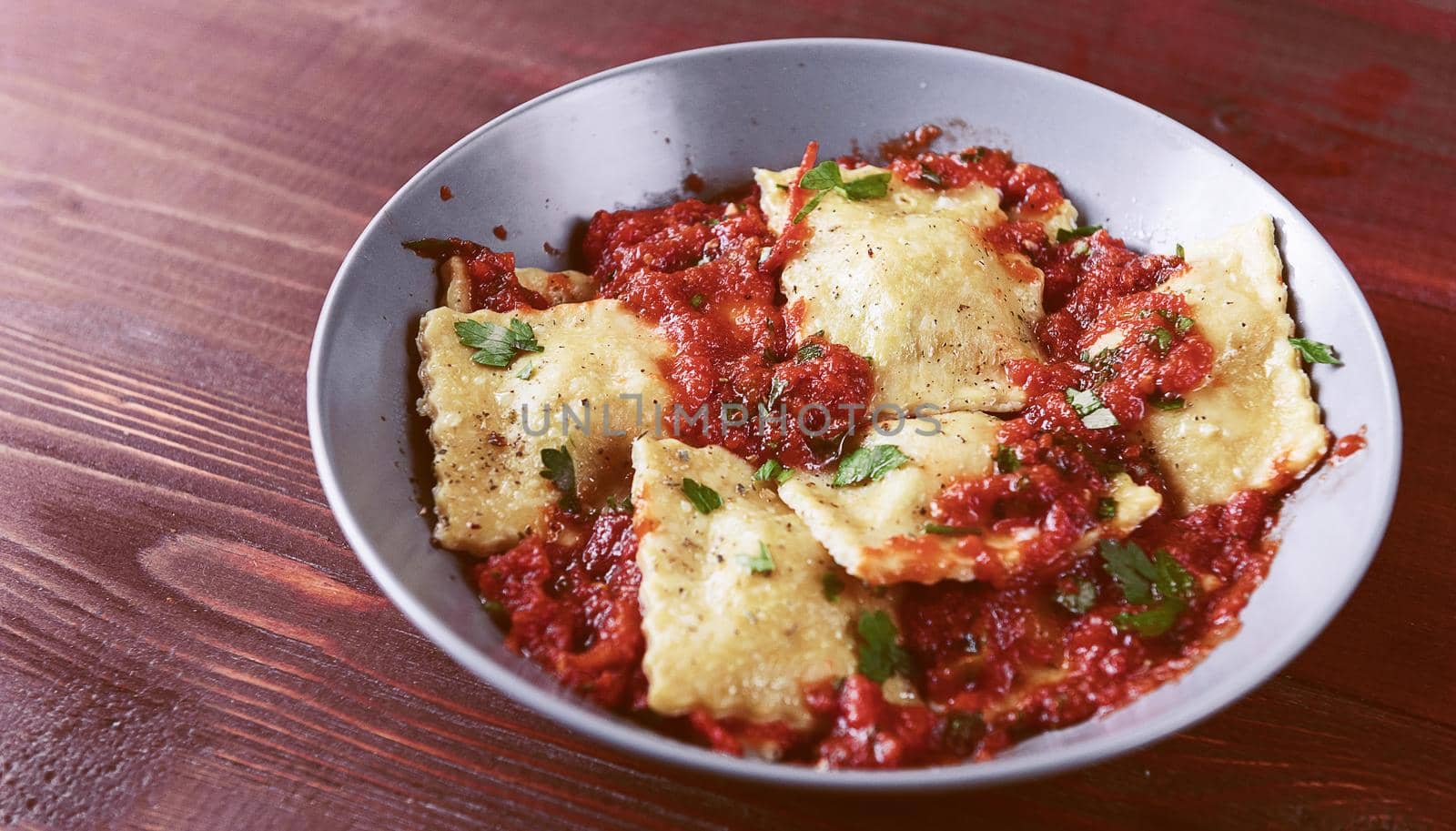 Delicious ravioli with tomato sauce in a plate on a wooden background