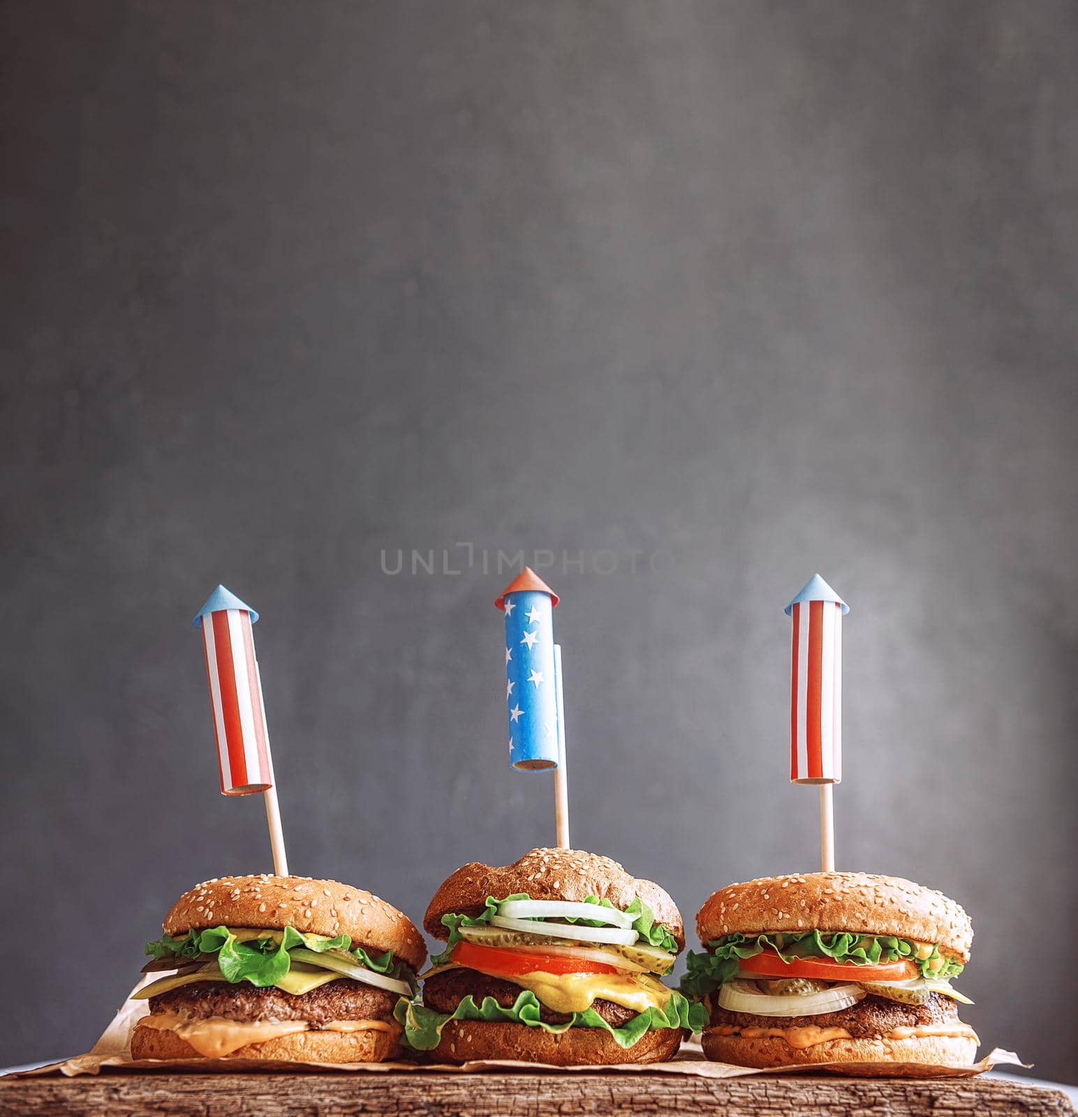 three fresh and juicy burgers with American flag-style fireworks inserted into them. barbecue concept picnic to celebrate independence day by vvmich