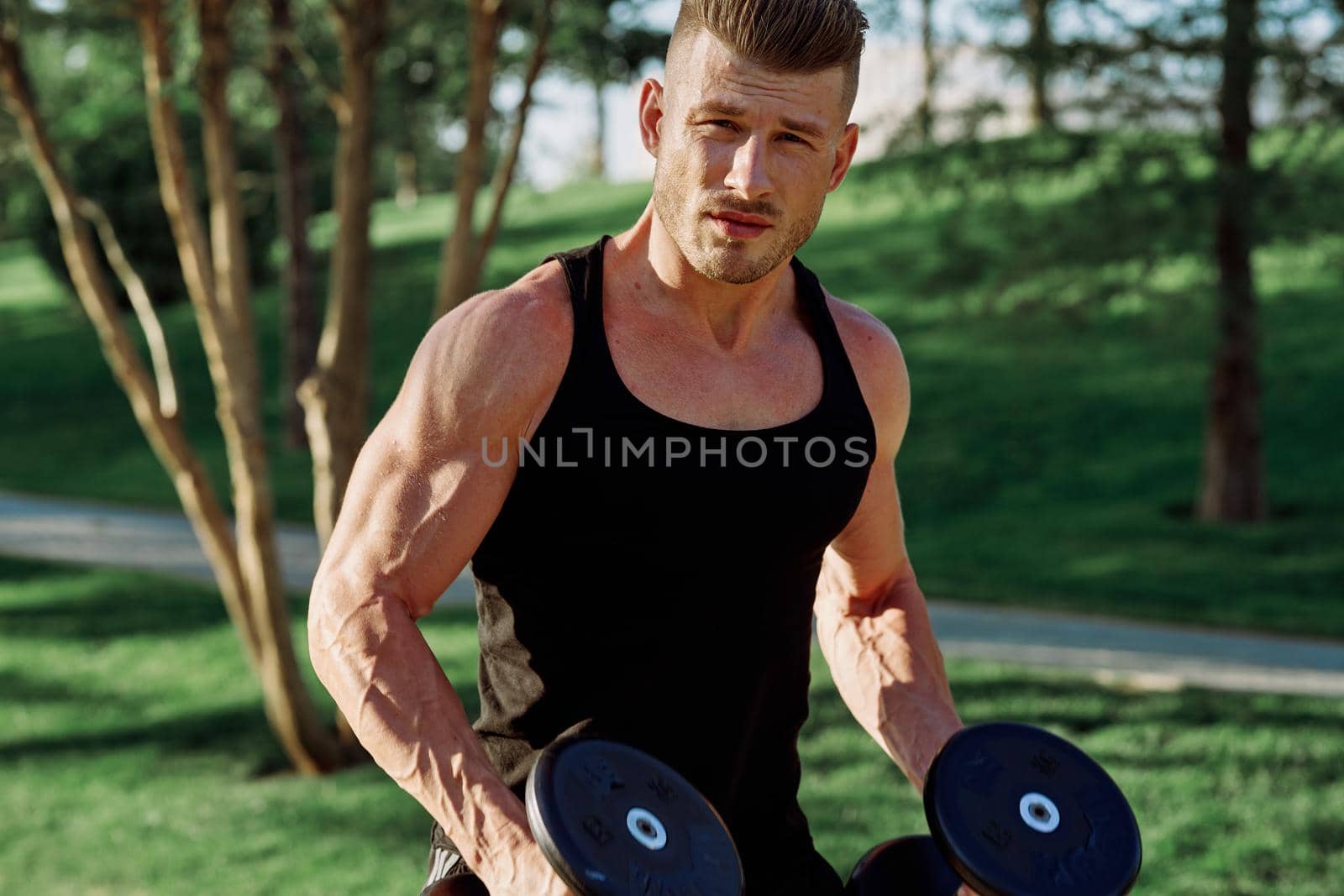 athletic man in black t-shirt with dumbbells in the park training. High quality photo