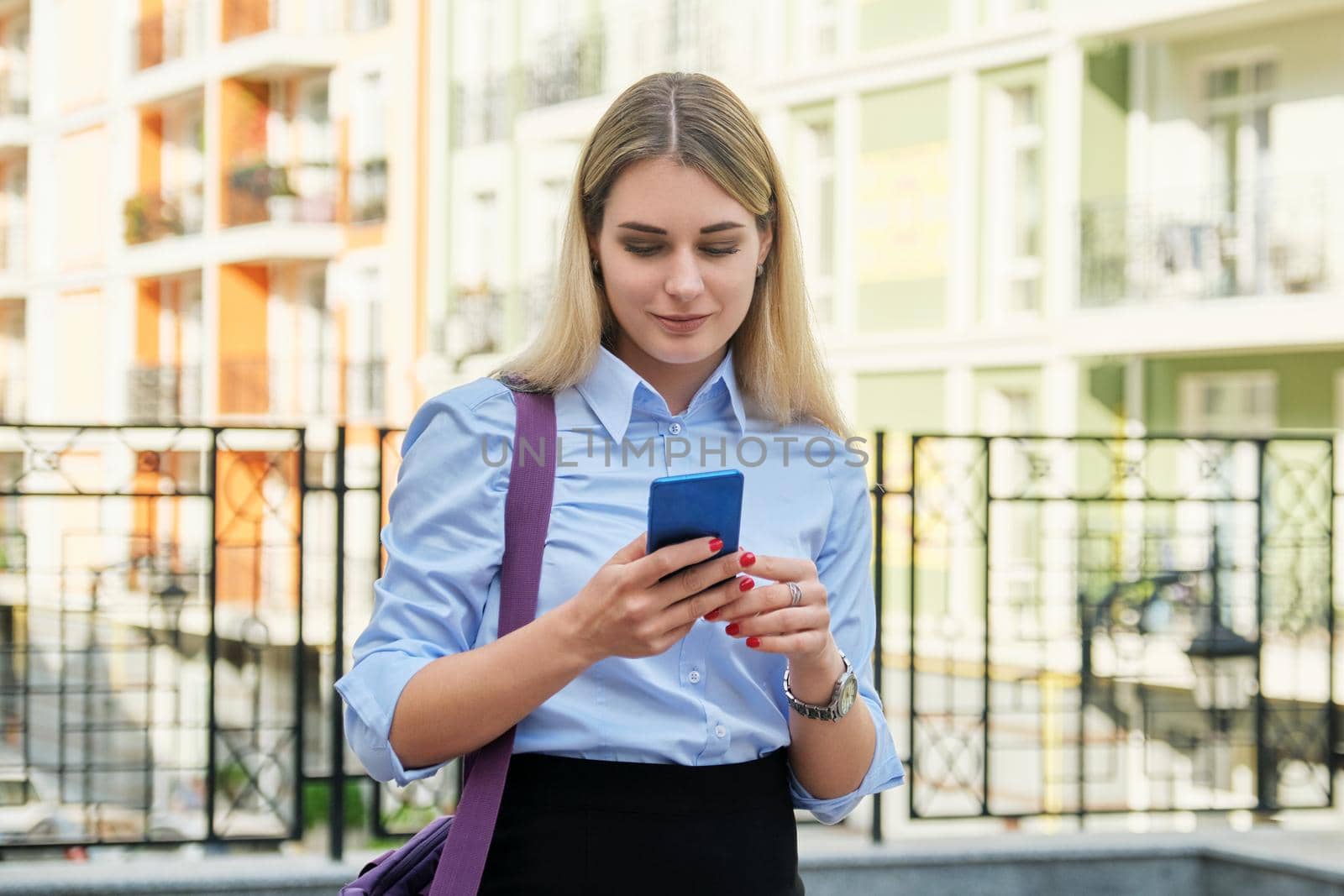 Young businesswoman with smartphone outdoor, street office building background