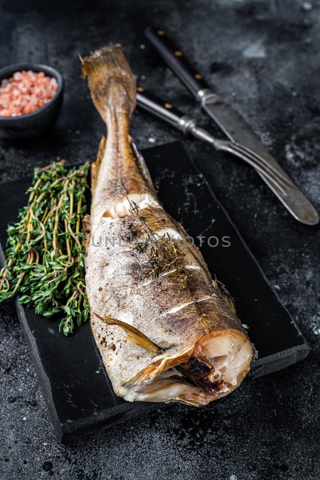 Roasted cod white fish with thyme on marble board. Black background. Top view.