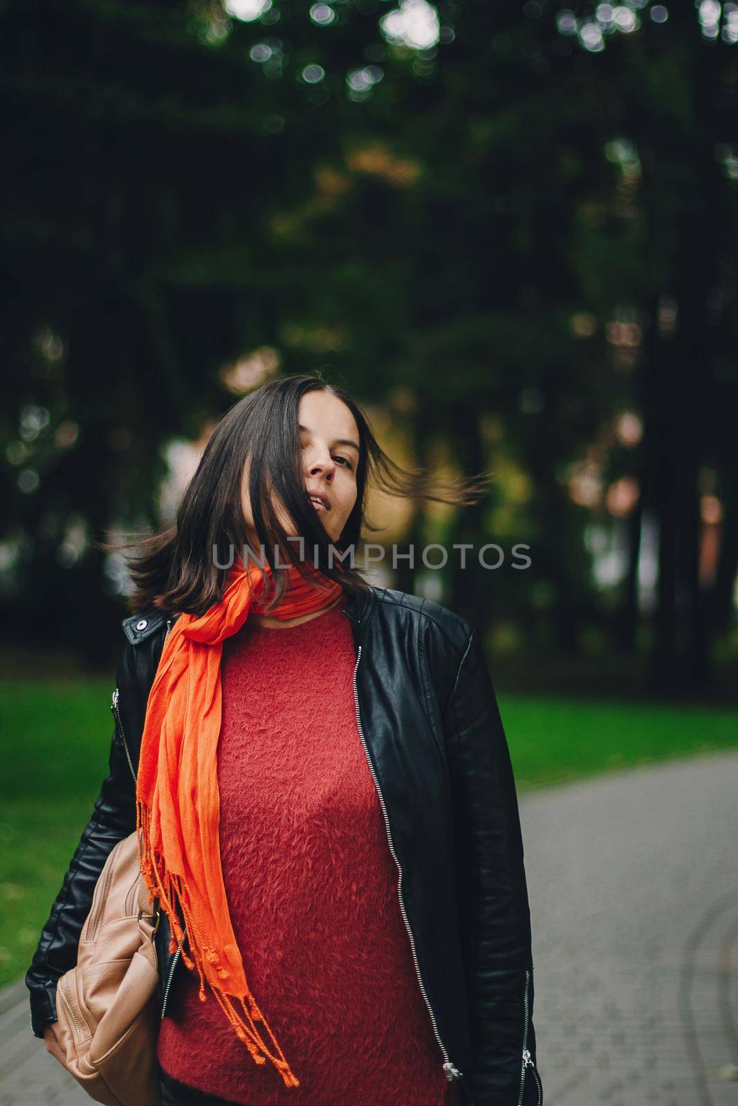 Portrait of a happy woman playing with bright orange scarf in the park
