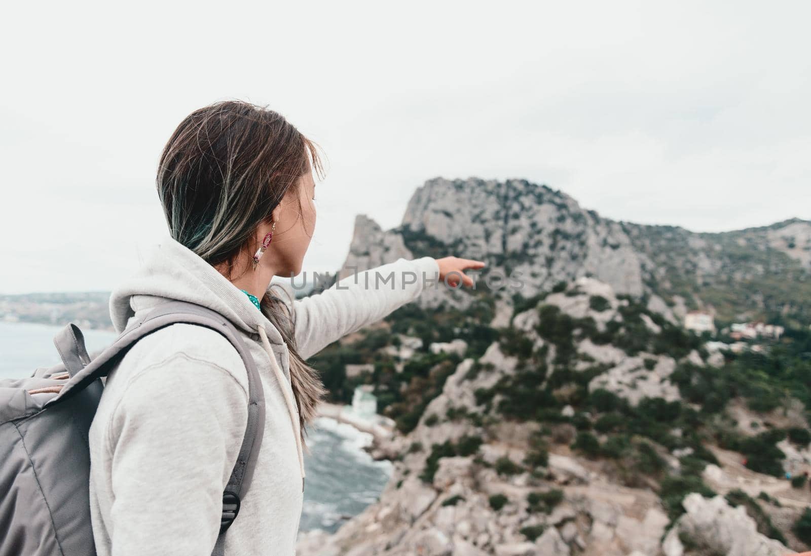 Explorer young woman with backpack pointing at cliff on coastline.