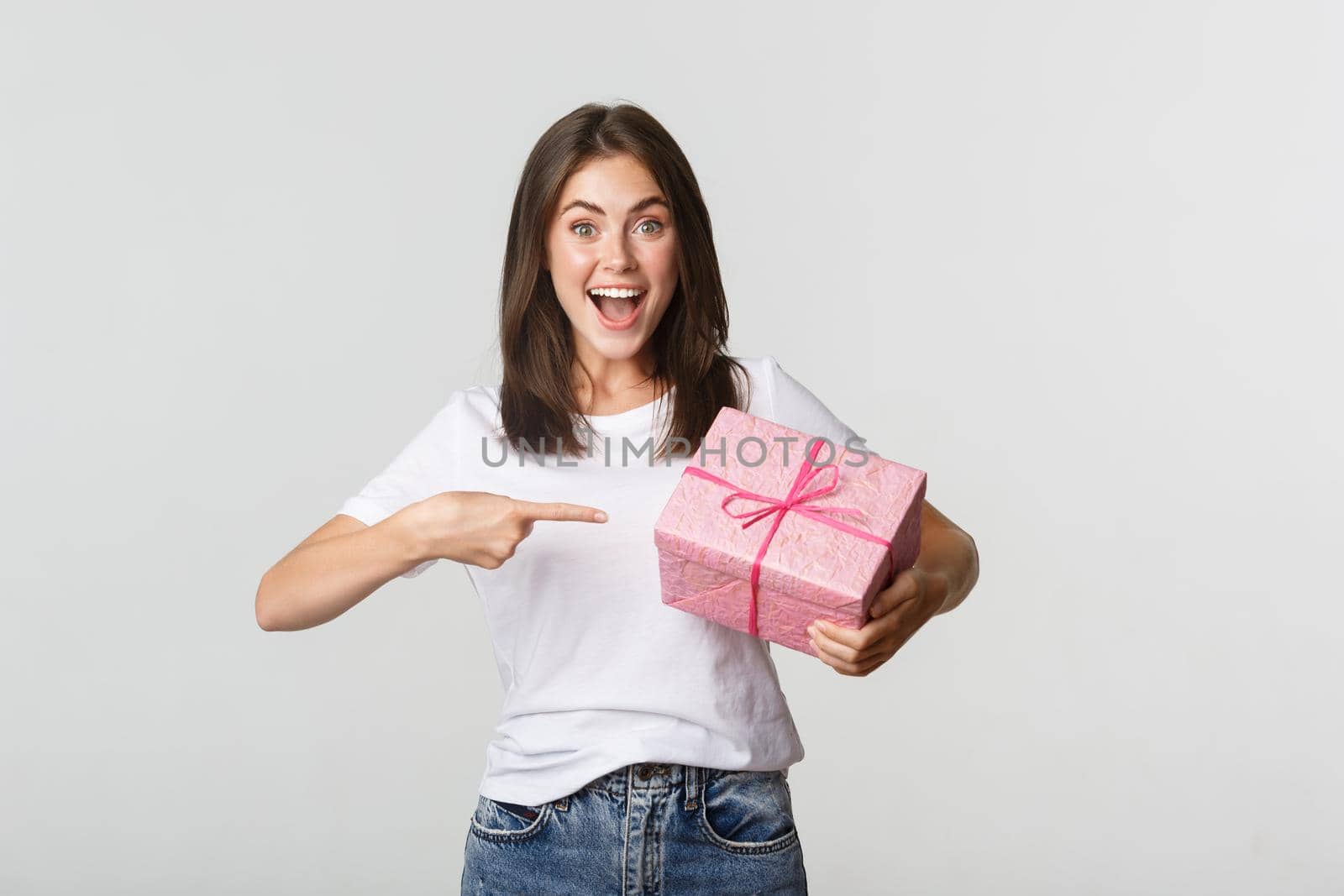 Surprised happy young woman smiling and pointing finger at wrapped gift.