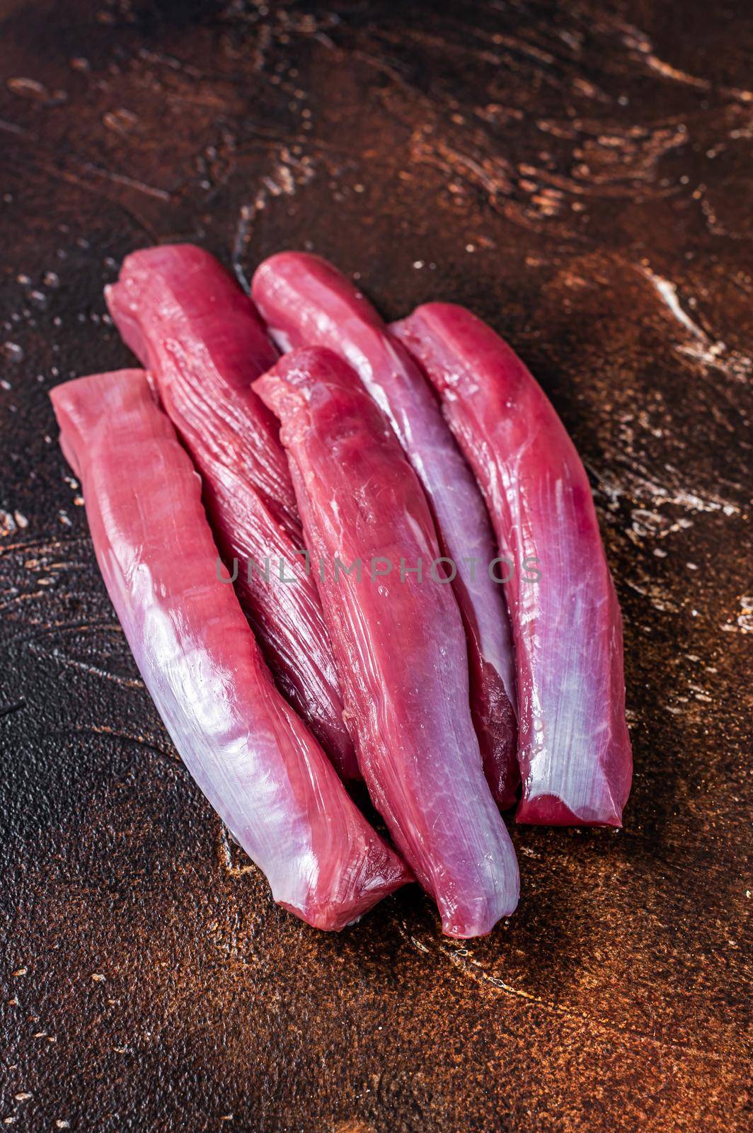 Raw lamb tenderloin meat on butcher table. Dark background. Top view.