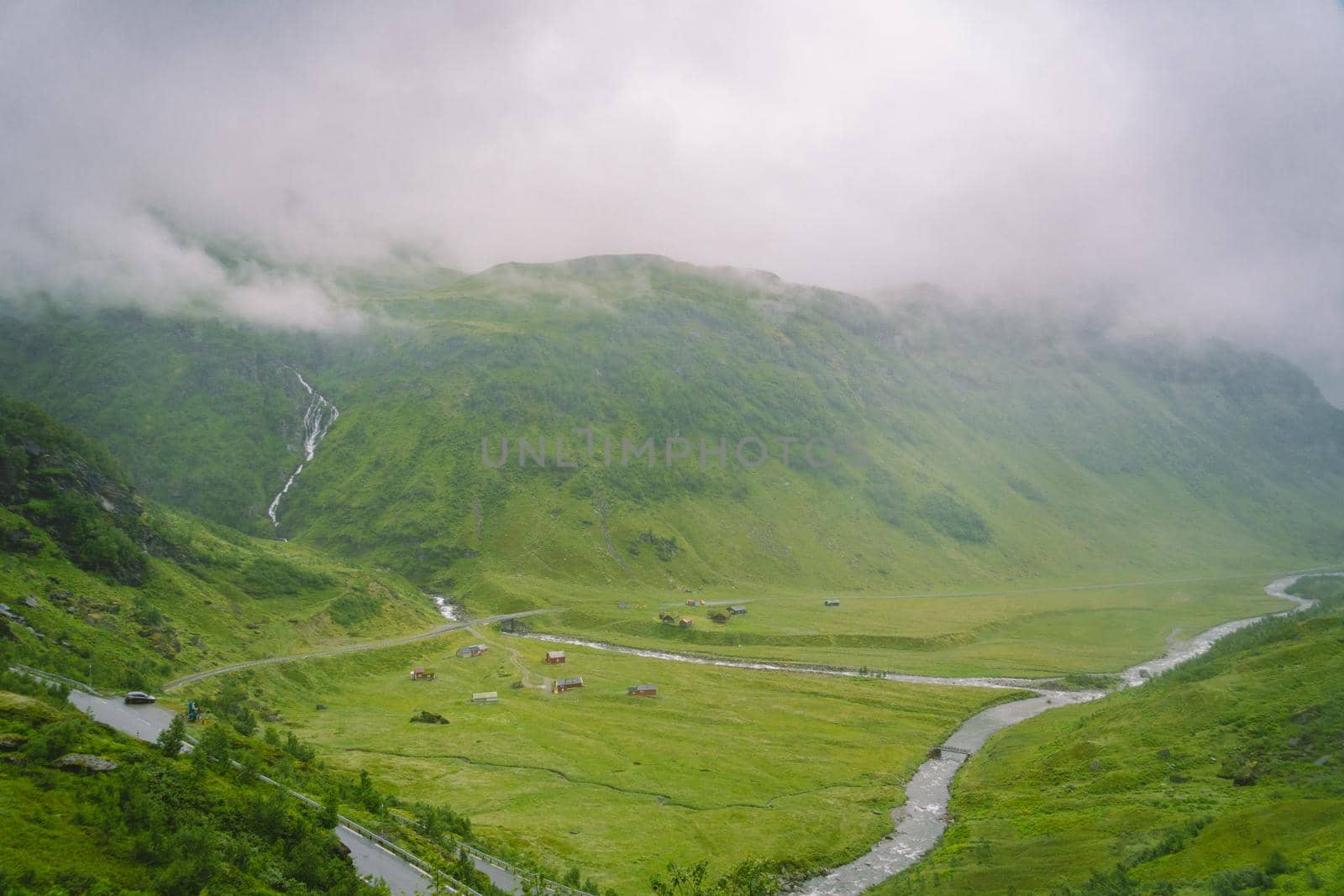Beautiful landscape and scenery view of Norway, green scenery hills and mountain in a cloudy day. green scenery of hills and mountain partially covered with fog. Farm and cottages on a glacier river by Tomashevska