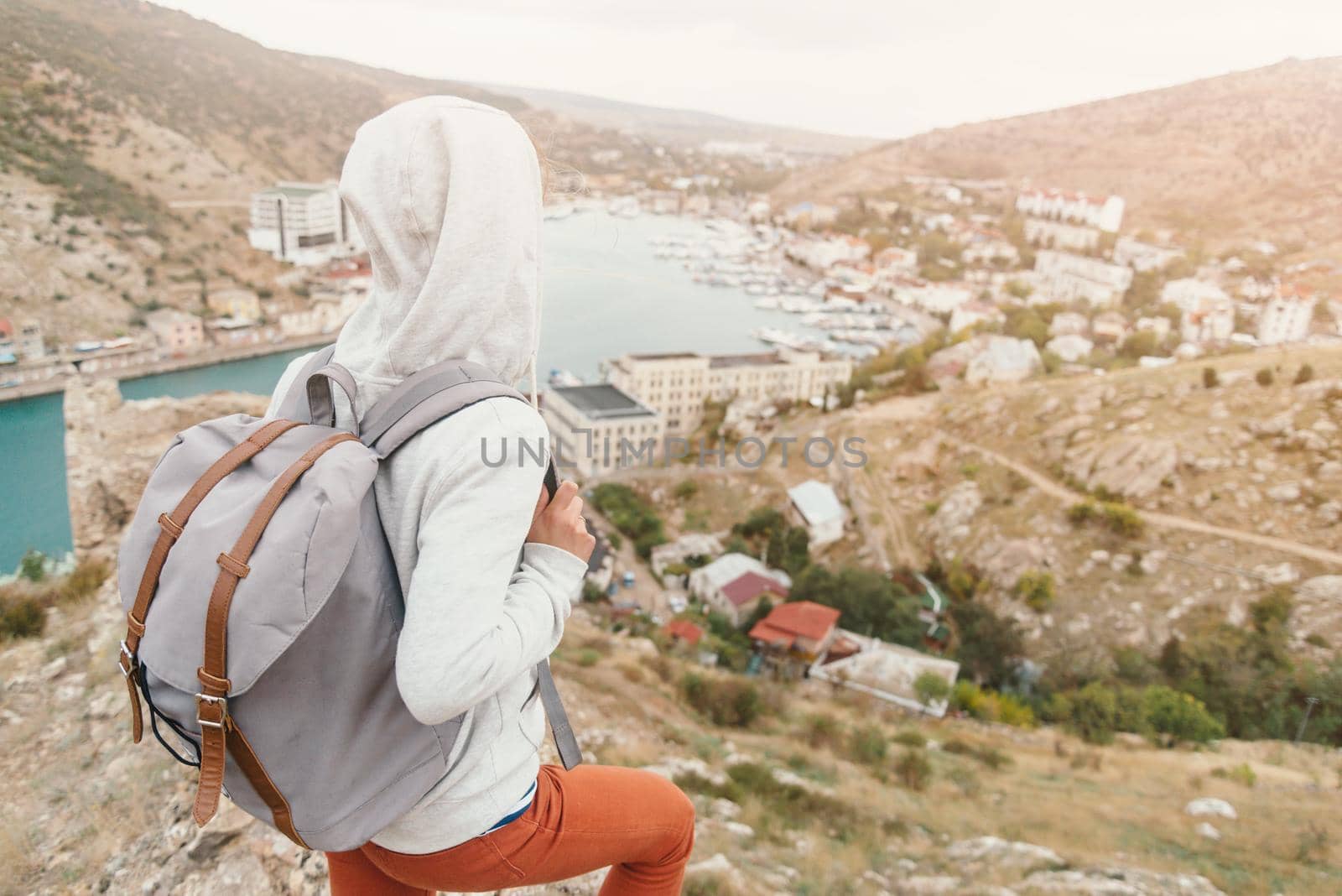 Unrecognizable female traveler with backpack looking at town about the bay.