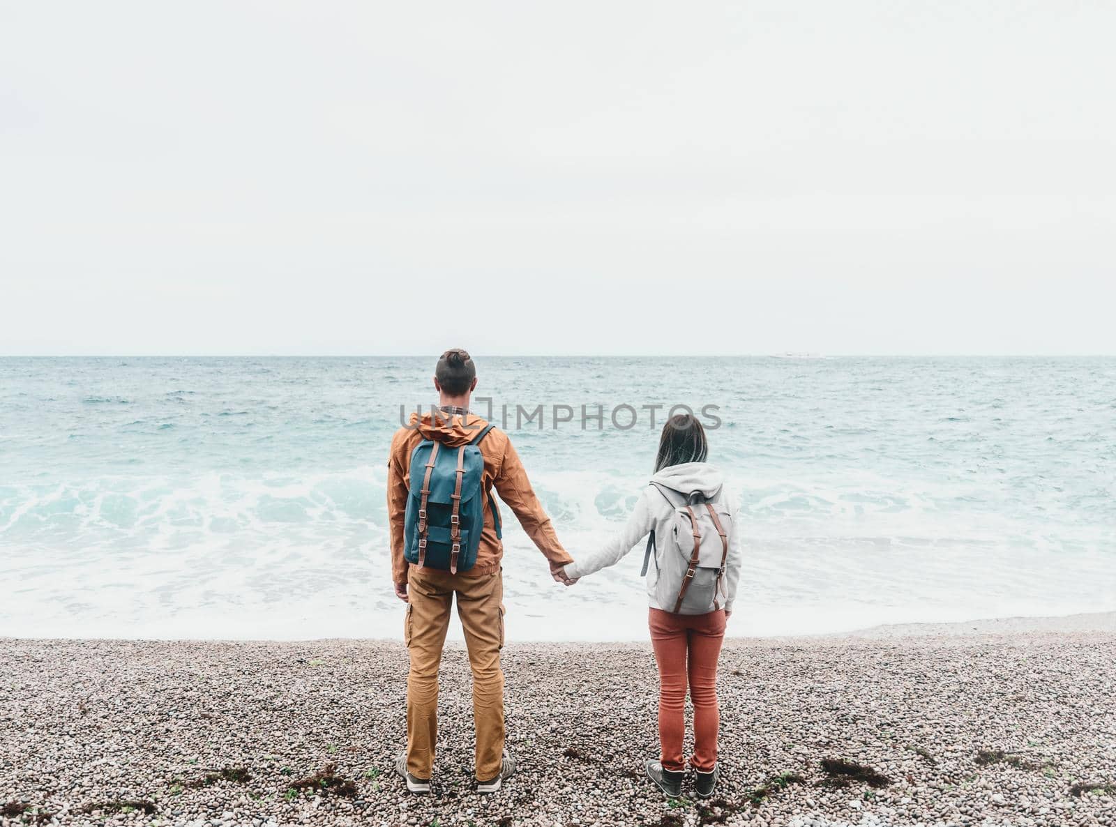 Traveler backpacker young couple in love standing on shore and enjoying view of sea.