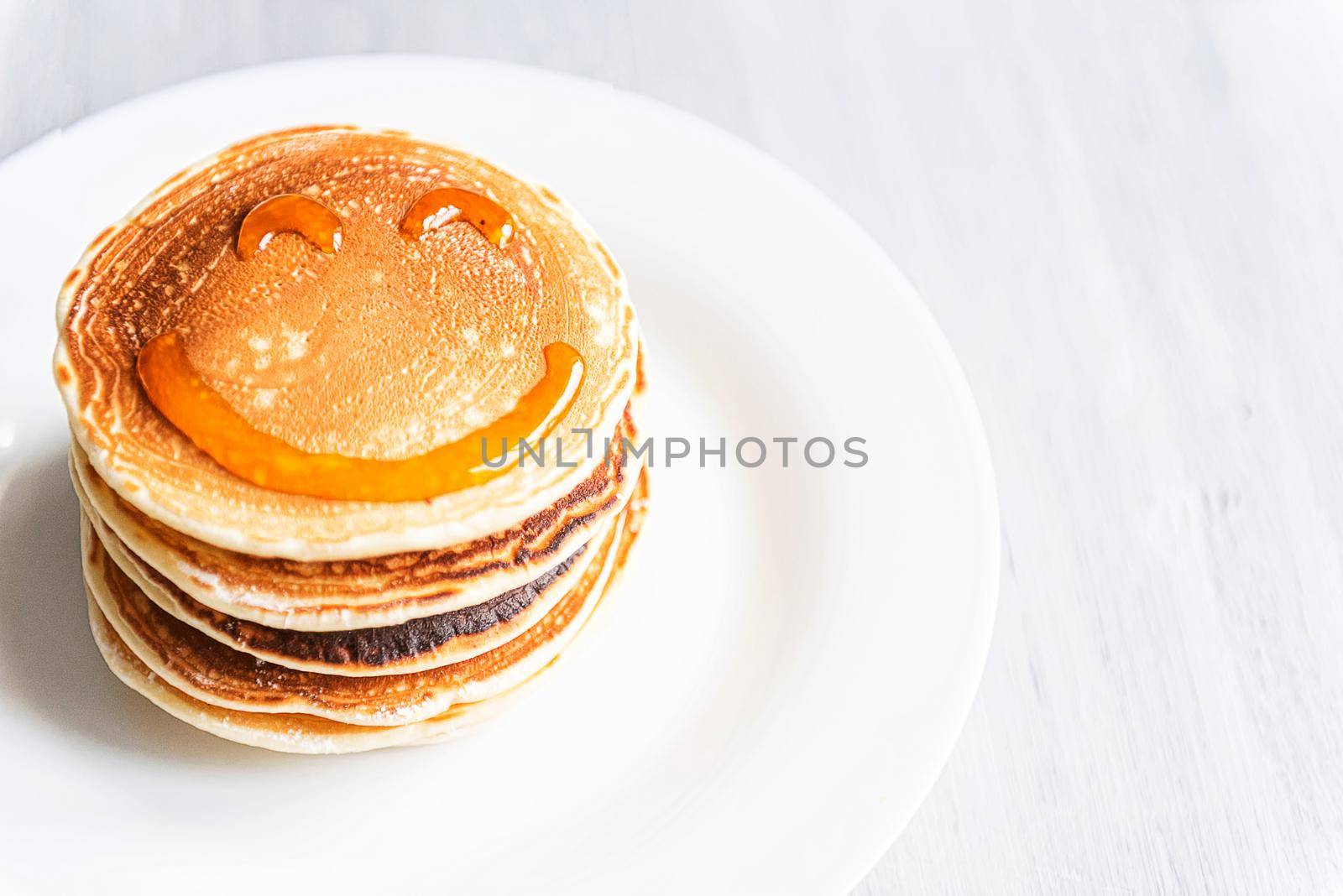 fresh classic pancake stacked in stack on gray background with place for text. with a smile painted with honey and maple syrup by vvmich