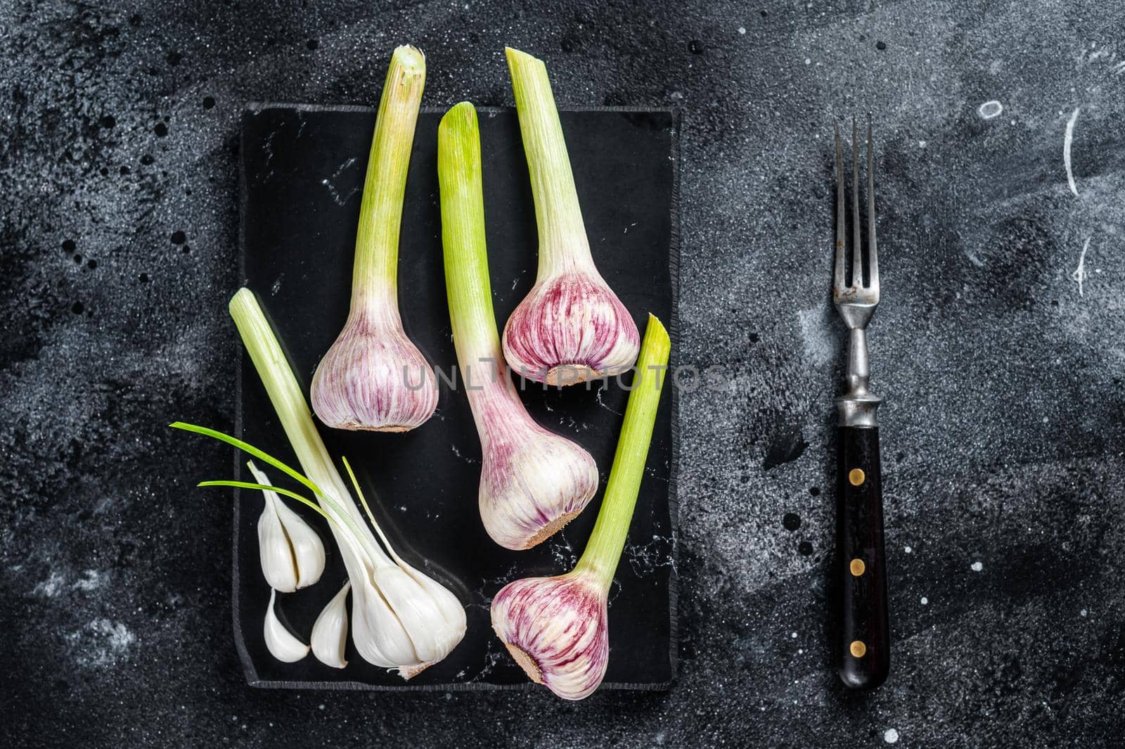 Raw Spring young garlic bulbs and cloves on marble board. Black background. Top view.