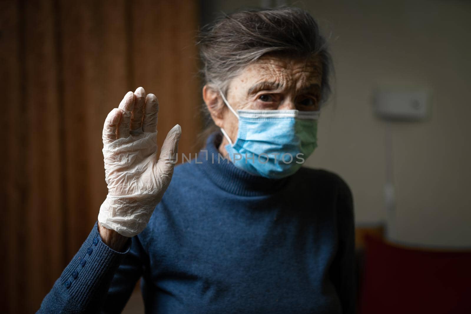 Importance wearing gloves and masks to protect of coronavirus, especially elderly and seniors. Focus on latex gloves on background old woman in medical mask. Sign indicates protection against covid 19