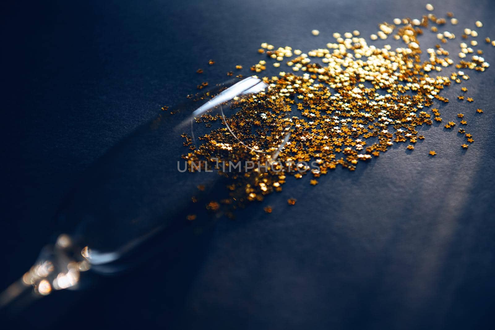 concept spilled white wine or champagne. end of the party. a glass of wine lying on a table in it gold stars symbolizing spilled wine