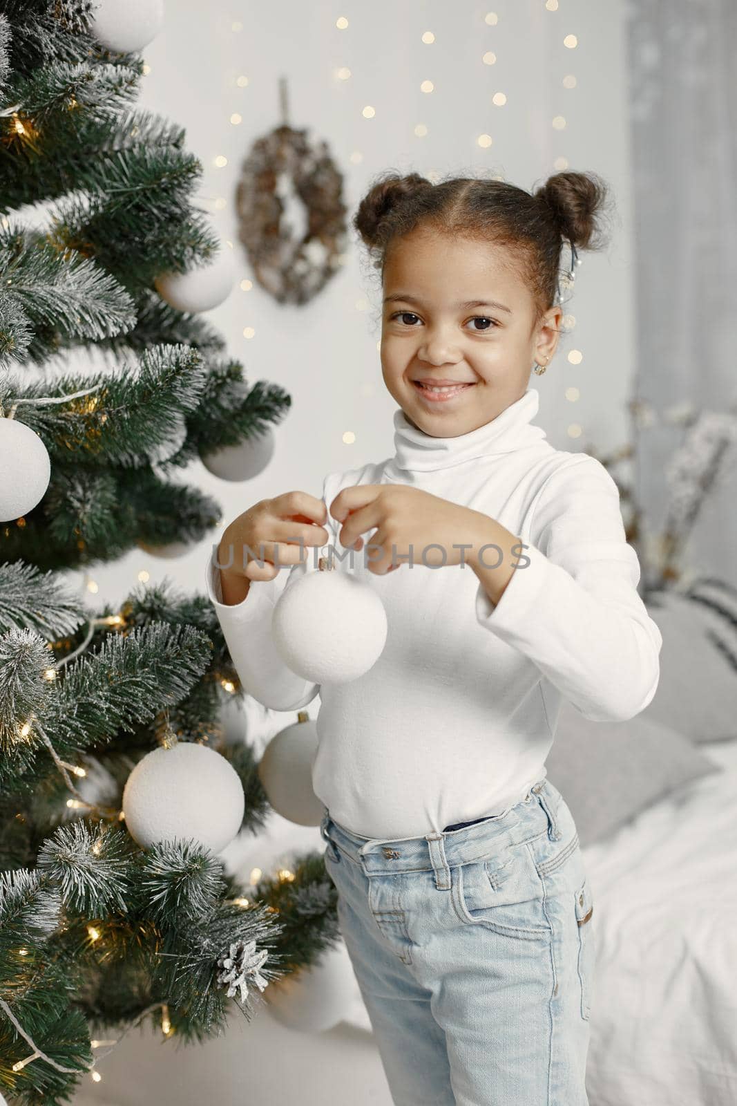 Child in a white sweater. Daughter standing near Christmas tree.