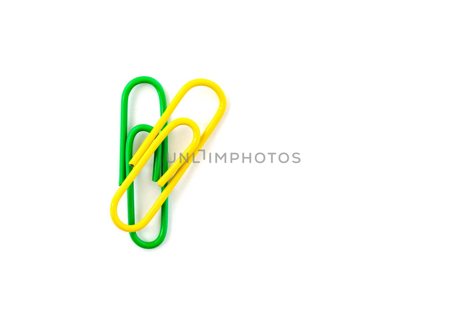 Green and yellow paper clip isolated on white background. Close up and top view