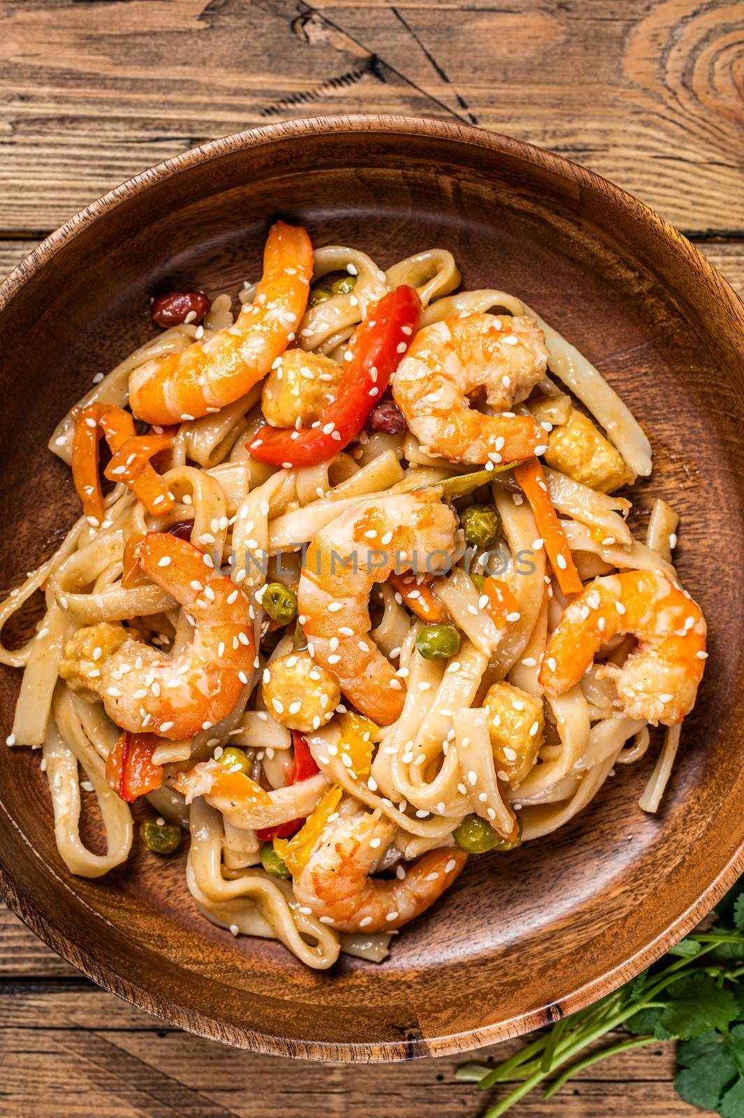 Udon stir-fry noodles with shrimp prawns in a wooden bowl. wooden background. Top view.