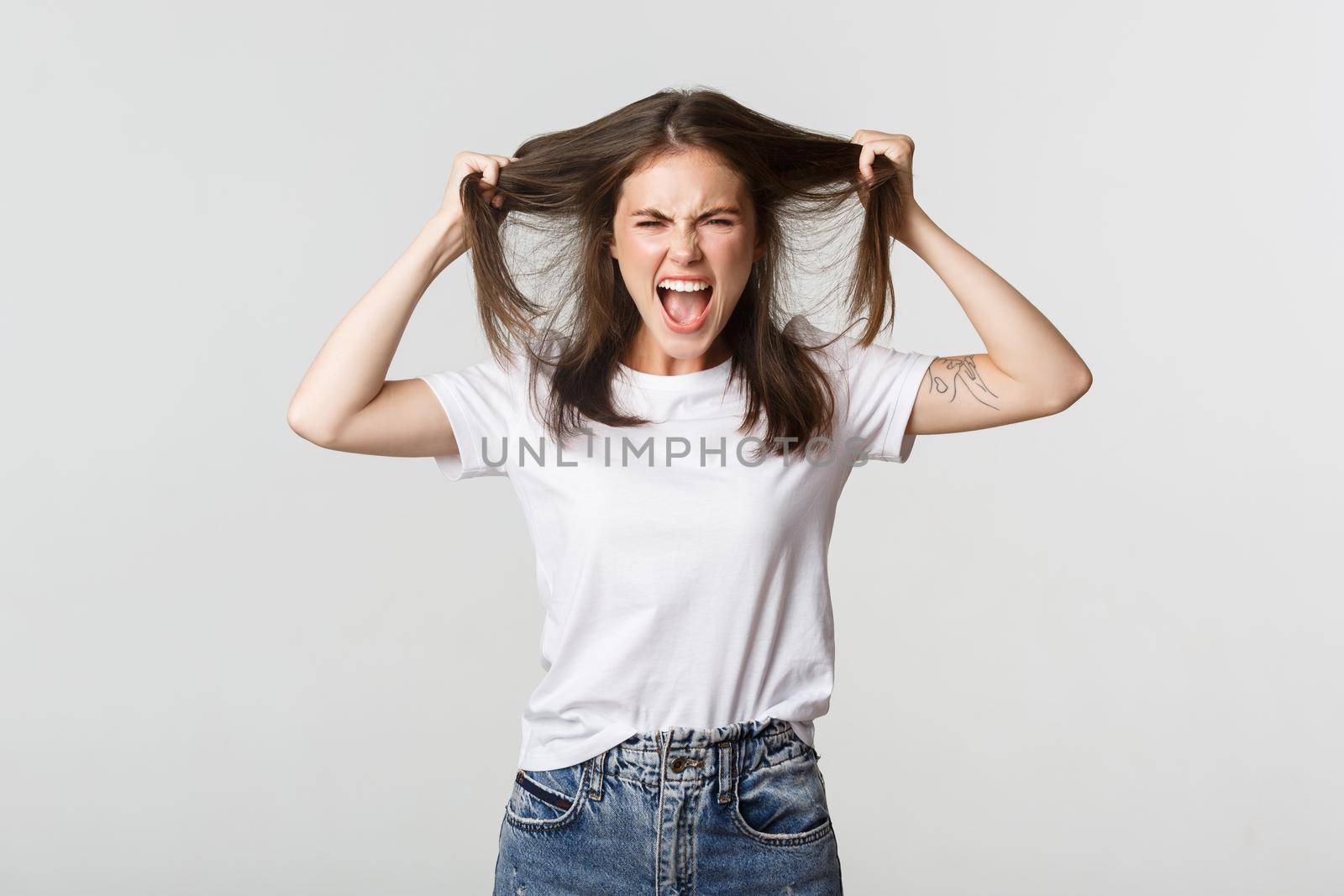 Outraged mad young woman ripping hair on head and yelling angry.