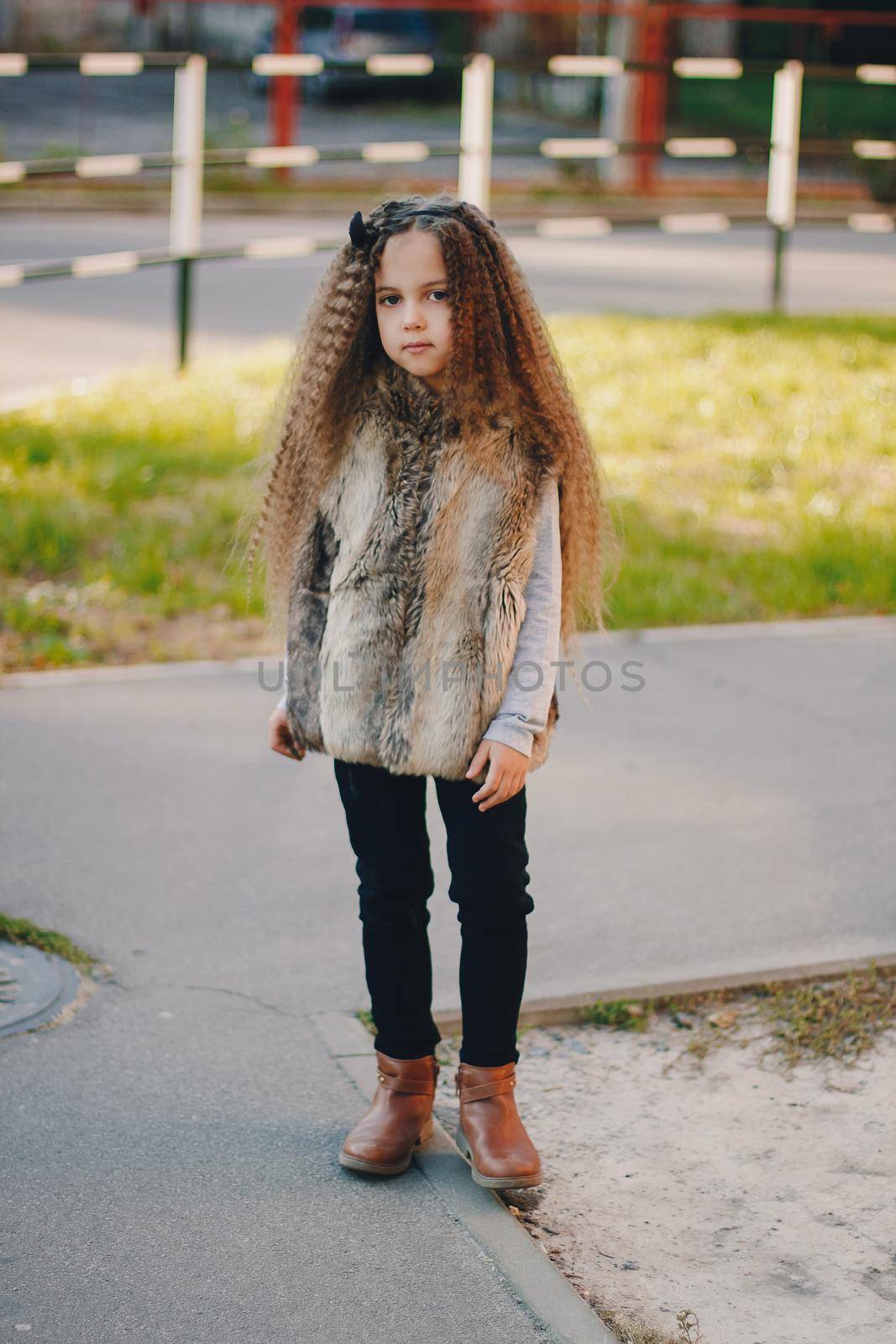 Stylish baby girl 4-5 year old wearing boots, fur coat, moving and playing. Autumn fall season.