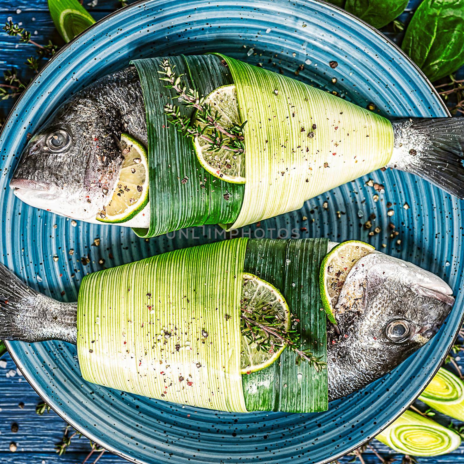 two fresh raw dorado fish, wrapped in palm leaves, sprinkled with a mixture of peppers and large gimolais salt, with slices of lime and lemon, ready to be baked. cooking dinner concept for two