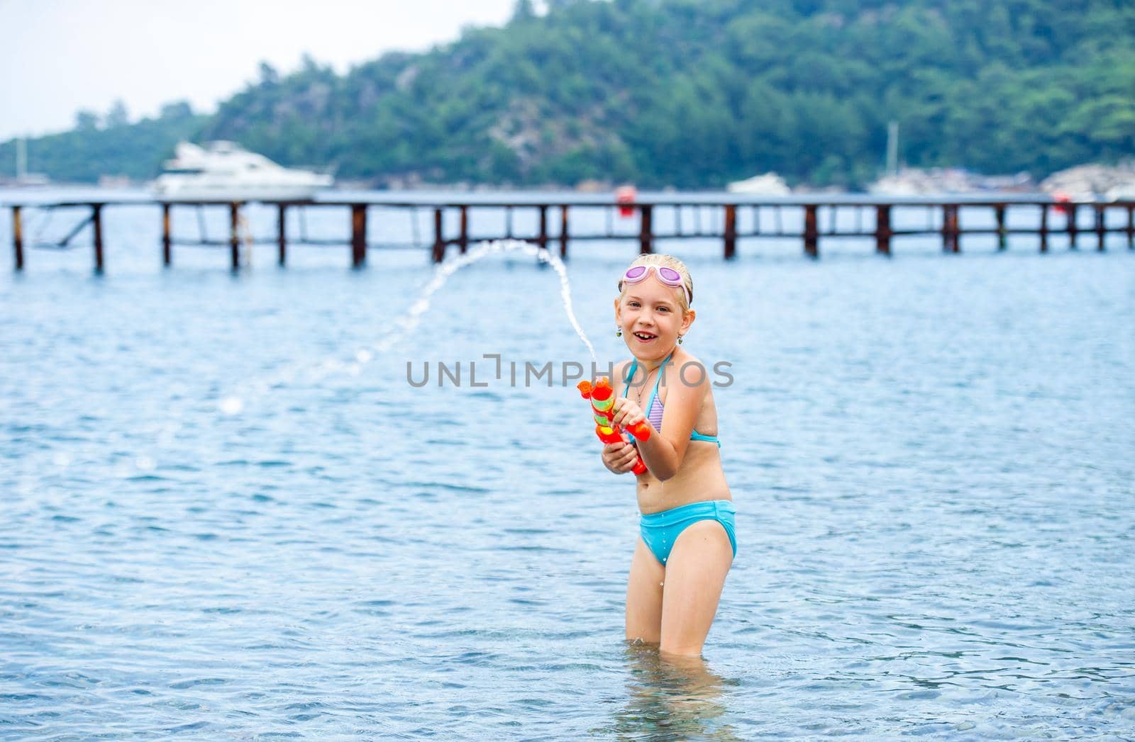Adorable little girl is swimming in the sea and playing with a water gun. Turkey.
