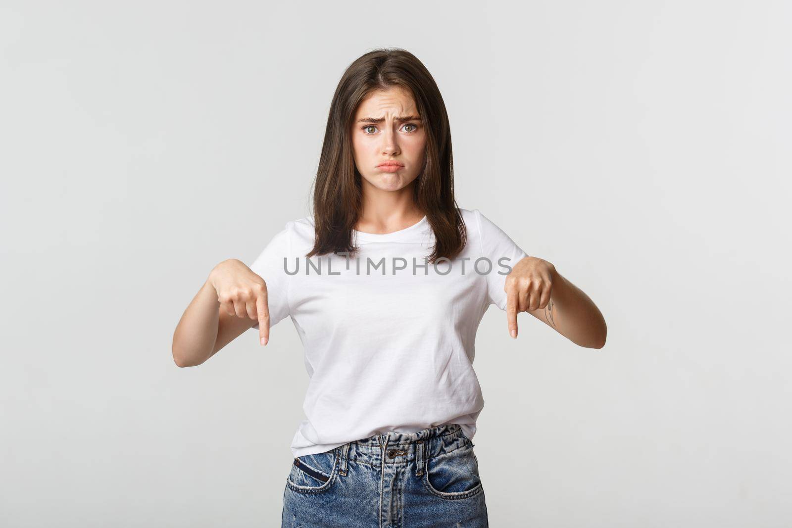 Sad and gloomy brunette girl sulking, pointing fingers down with regret.