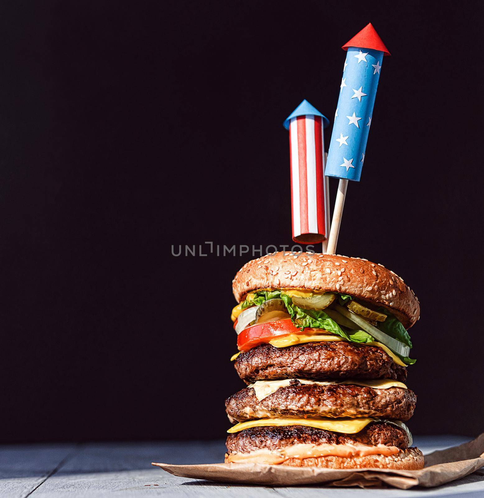 a big burger with three juicy beef patties bonded with American flag firework skewers. burgar concept for the day of independence day celebration of fourth of july by vvmich