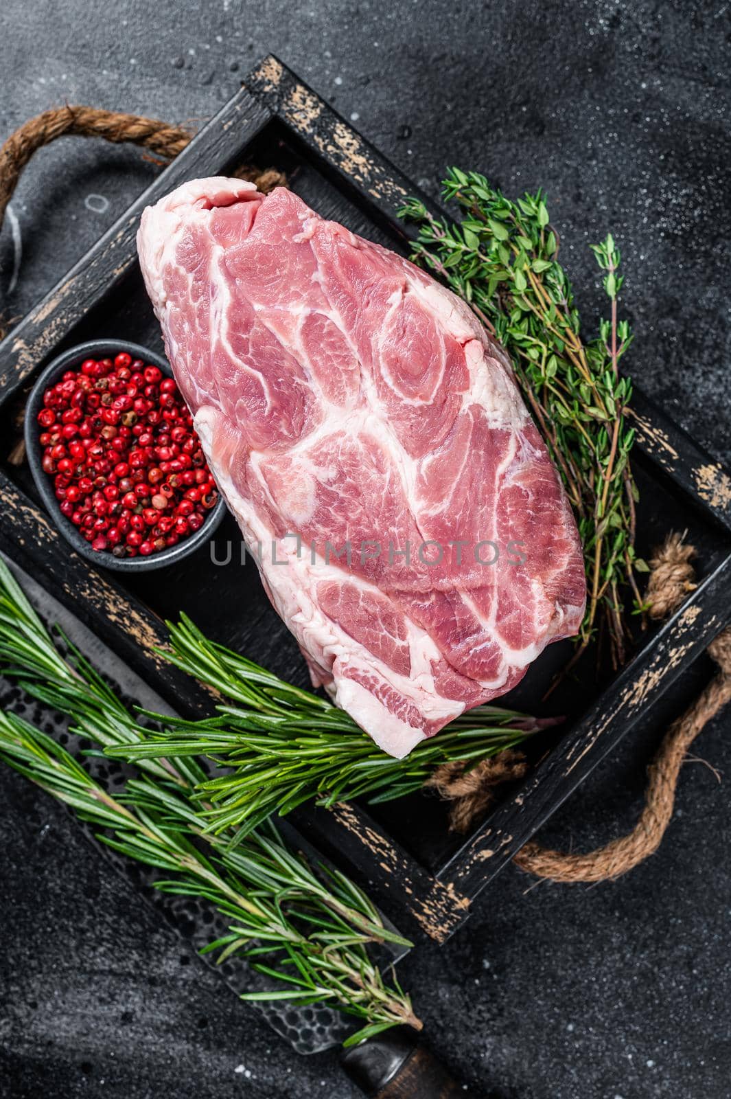 Raw pork neck meat piece for Chop steak in wooden tray with herbs. Black background. Top view.
