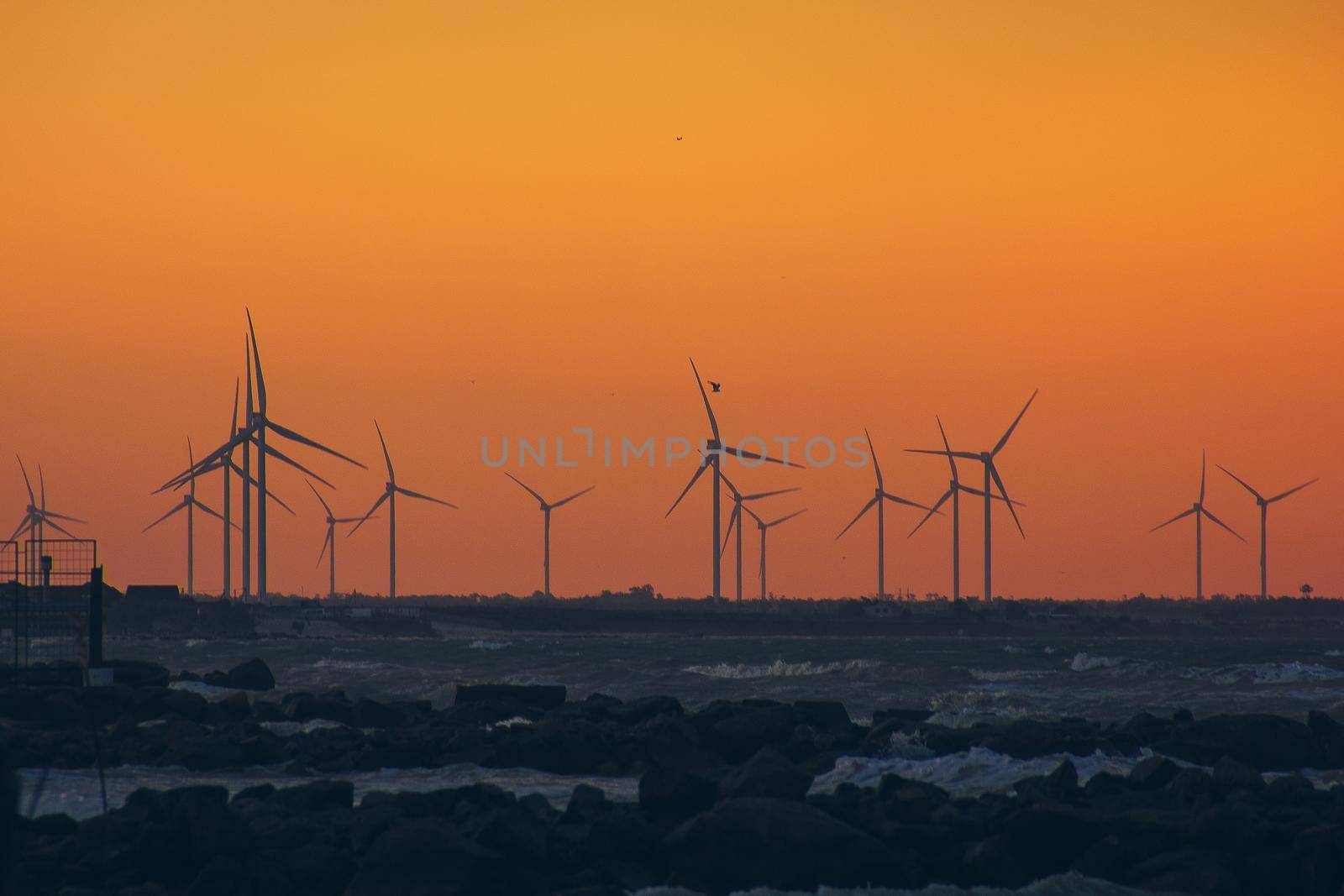 Wind turbine power generators silhouettes at ocean coastline at sunset. Alternative renewable energy production
