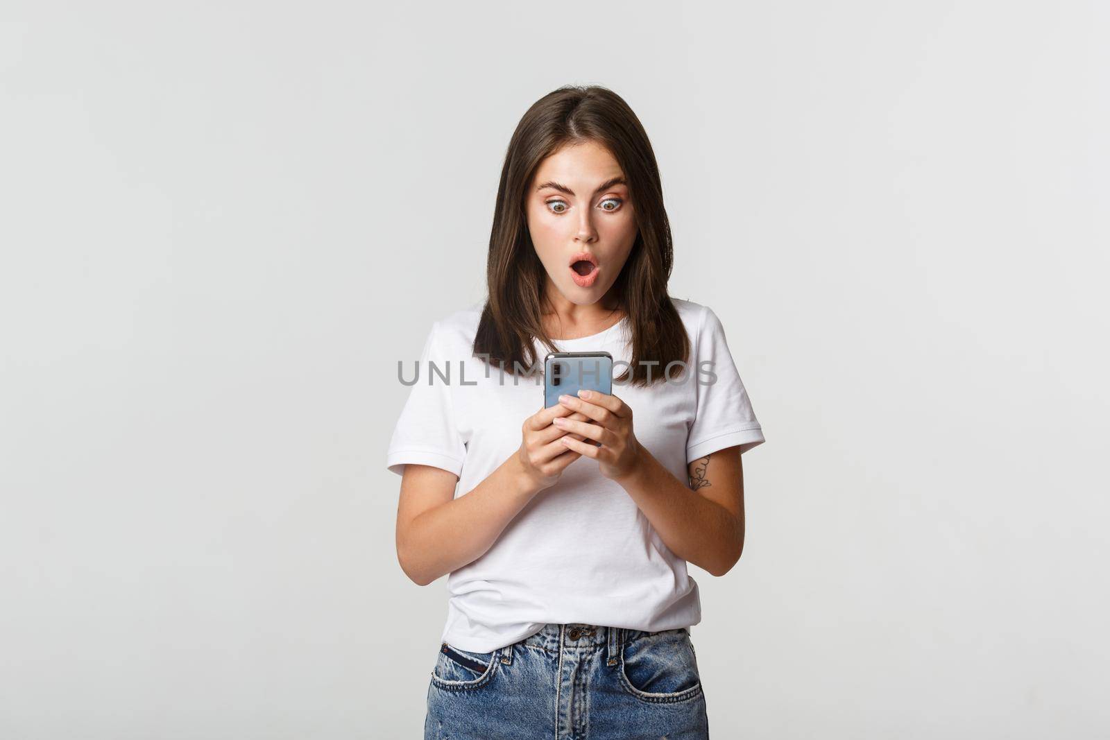Shocked and impressed brunette girl looking amazed at smartphone screen.