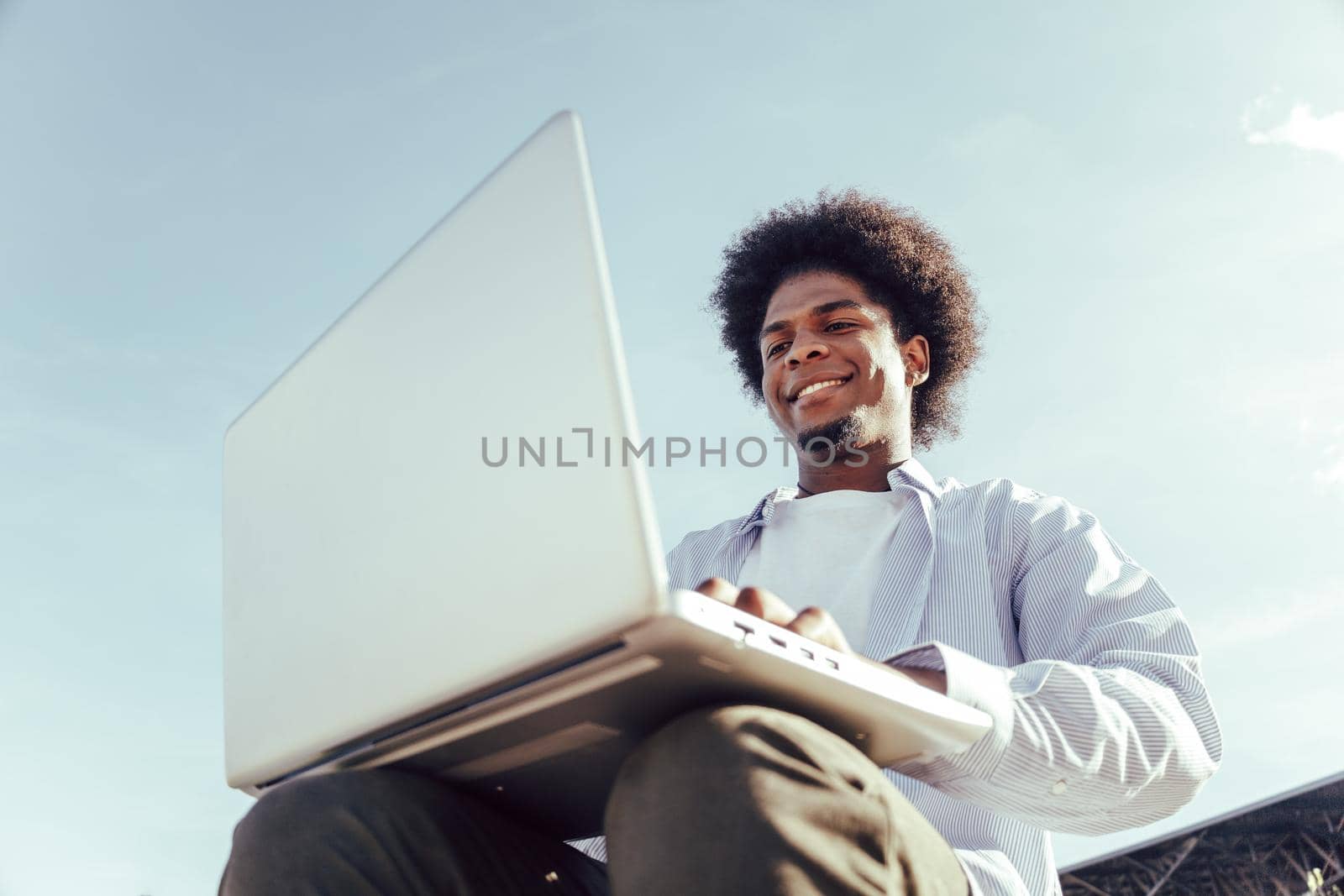 close up from below of young african student working in laptop outdoors by ALVANPH