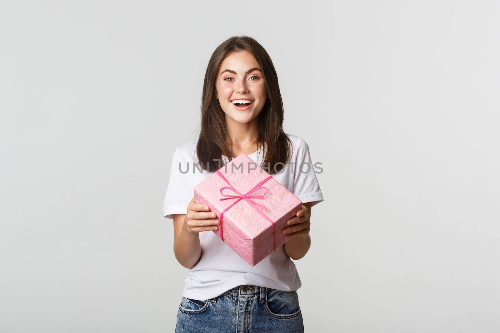 Attractive happy brunette girl holding birthday gift and smiling cheerful.