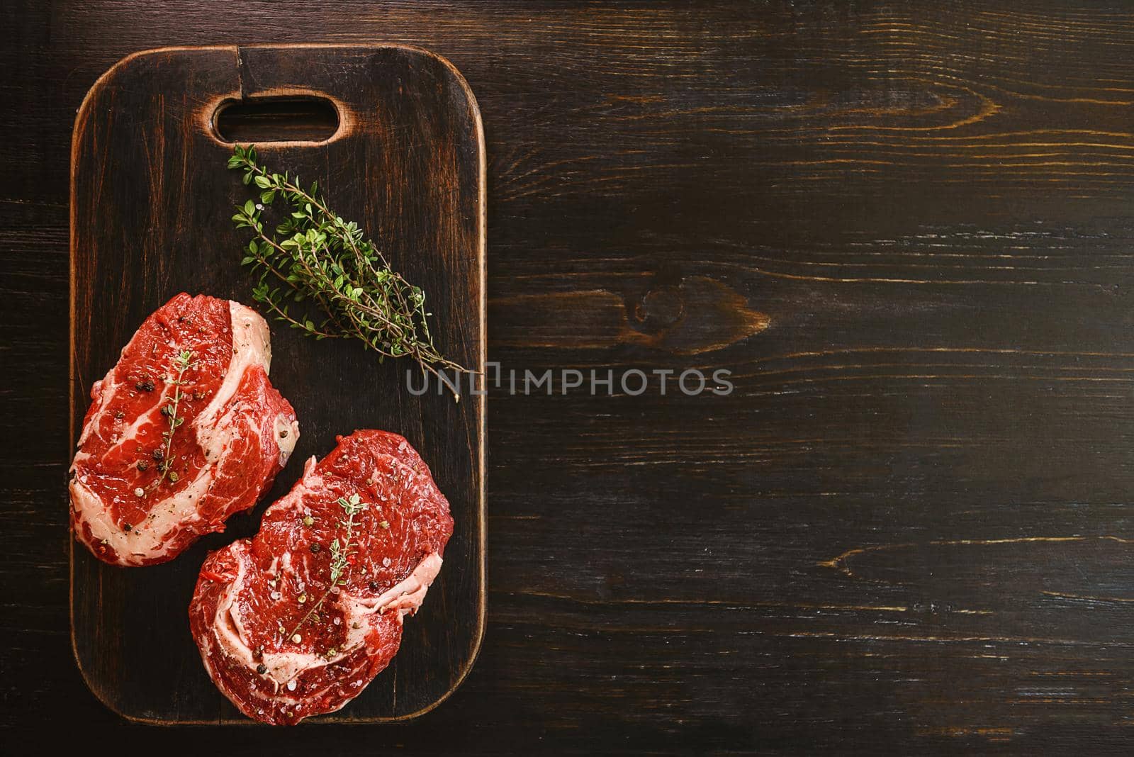 two raw marbled beef steaks in olive oil and spices ready for frying. dinner party concept by vvmich