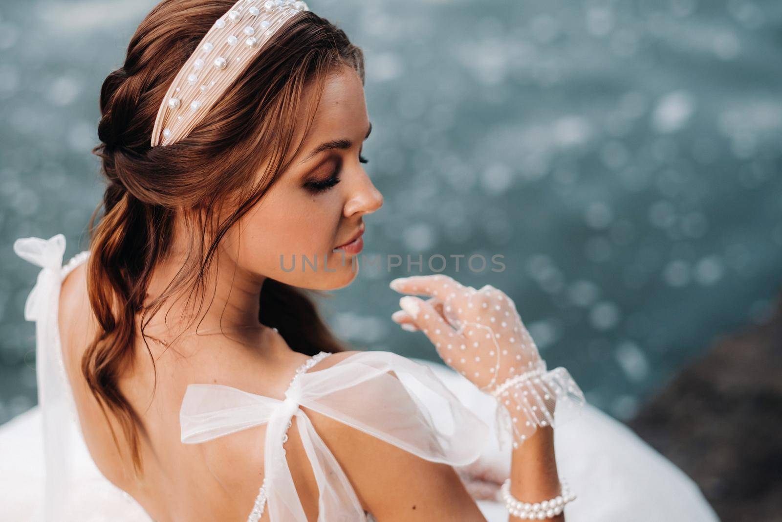 An elegant bride in a white dress and gloves is sitting by the lake in the Park, enjoying nature.A model in a wedding dress and gloves in a nature Park.Belarus