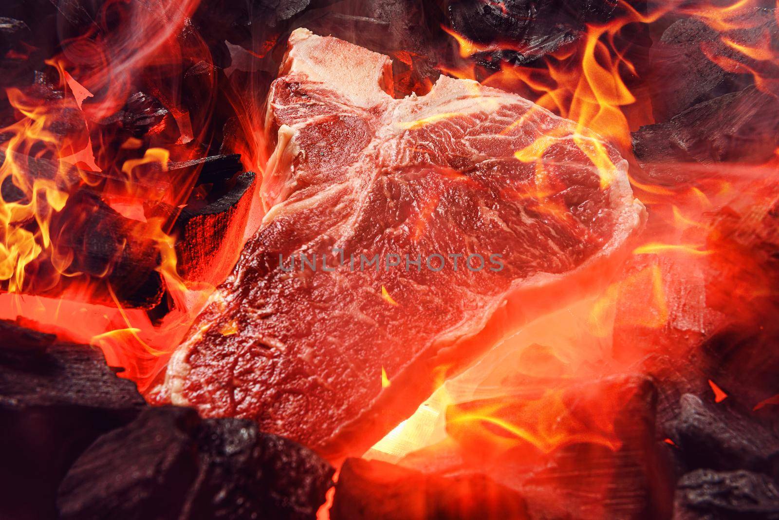 raw marbled beef steak with coals and smoke