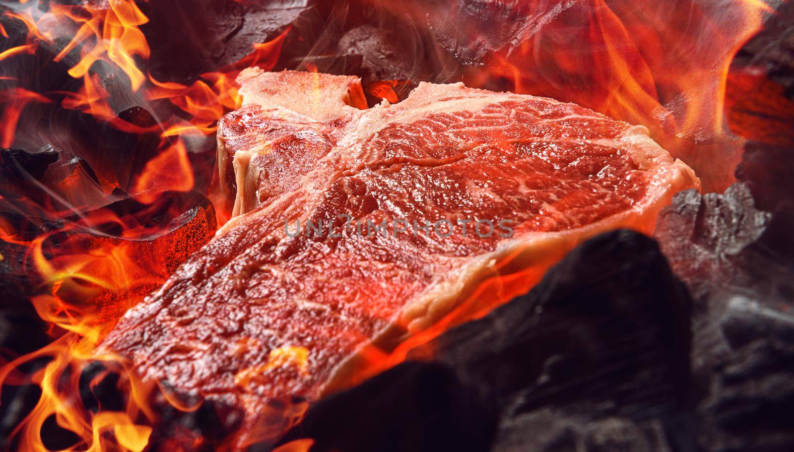 raw marbled beef steak with coals and smoke