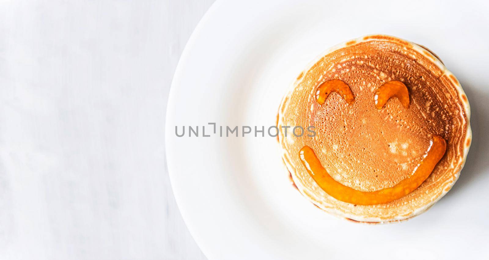 fresh classic pancake stacked in stack on gray background with place for text. with a smile painted with honey and maple syrup