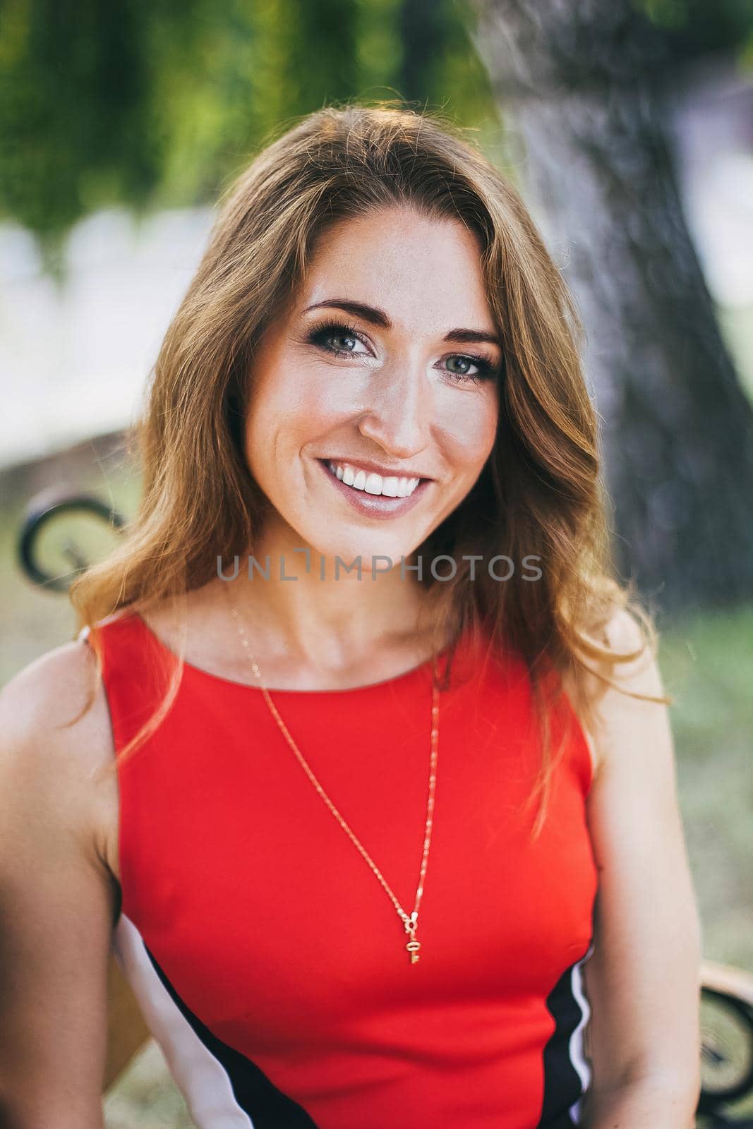 Beautiful smiling young woman girl looking at you in bright red dress outside.