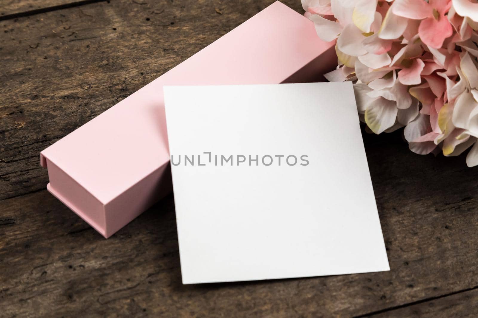 Pastel pink hydrangea flowers, gift box and a piece of paper on a wood background. Copy space for text.
