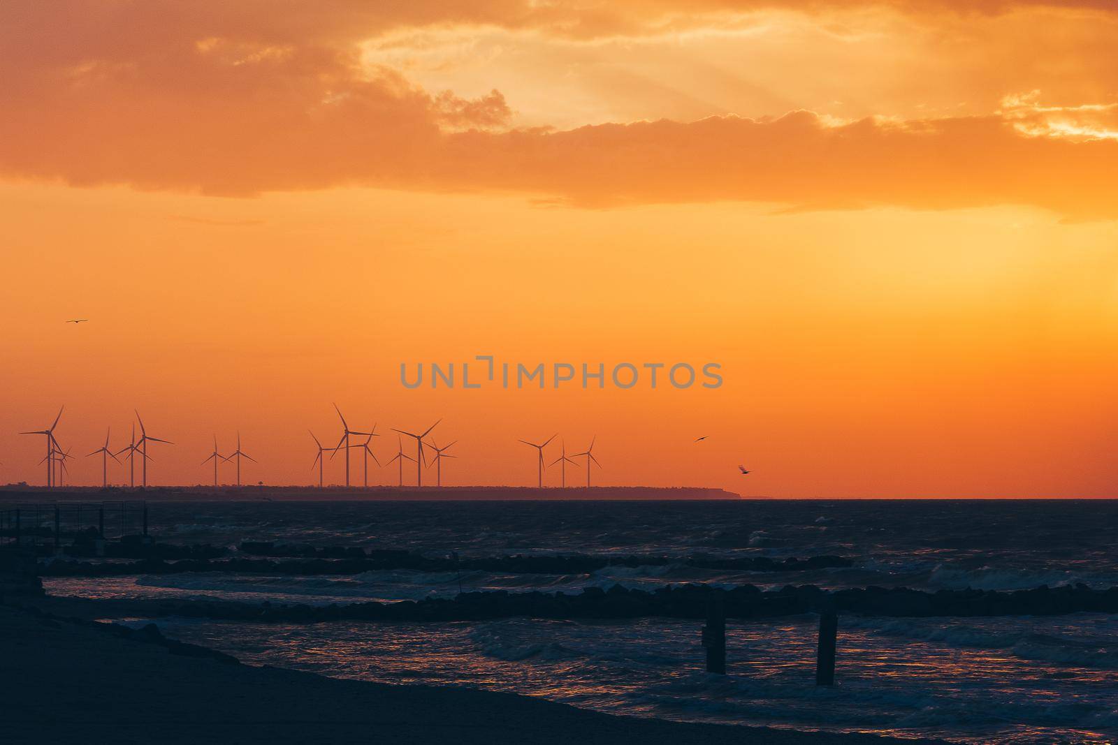 Wind turbine power generators silhouettes at ocean coastline at sunset. Alternative renewable energy production