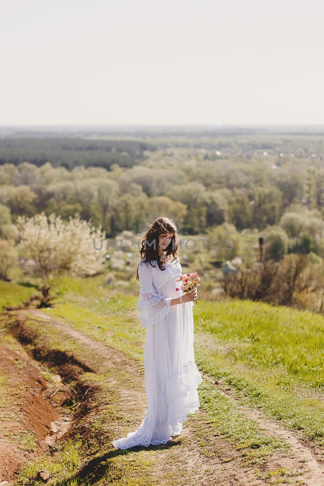 Portrait of carefree young woman in white vintage wedding style dress in spring cherry blossom garden valley.